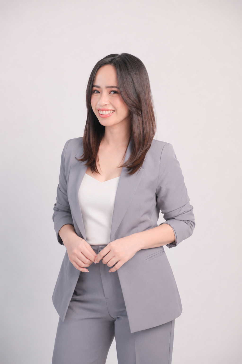 A clean, minimalist professional portrait of Dana Joy Camoit smiling warmly, dressed in a sharp grey blazer and trousers over a neutral cream top, projecting a trustworthy and modern corporate identity.